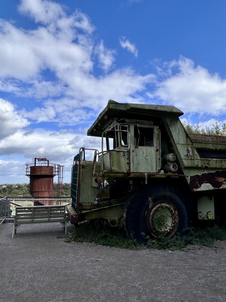 A very big green vehicle with patches of rust and vegetation growing around it.