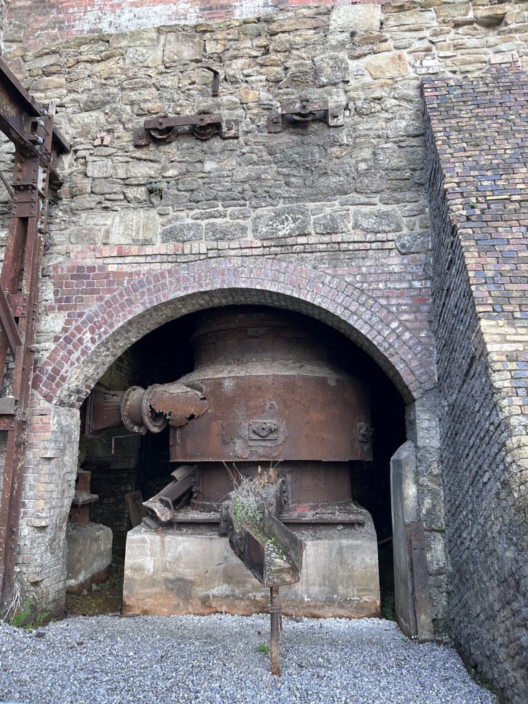 The remains of a metal machine set into the wall. An arch of old brickwork and a buttress of brick.
