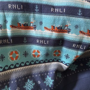 A close-up photo of a patterned jumper. The pattern shows lifeboats, snowflakes, anchors, waves, and life preservers in a repeated pattern.