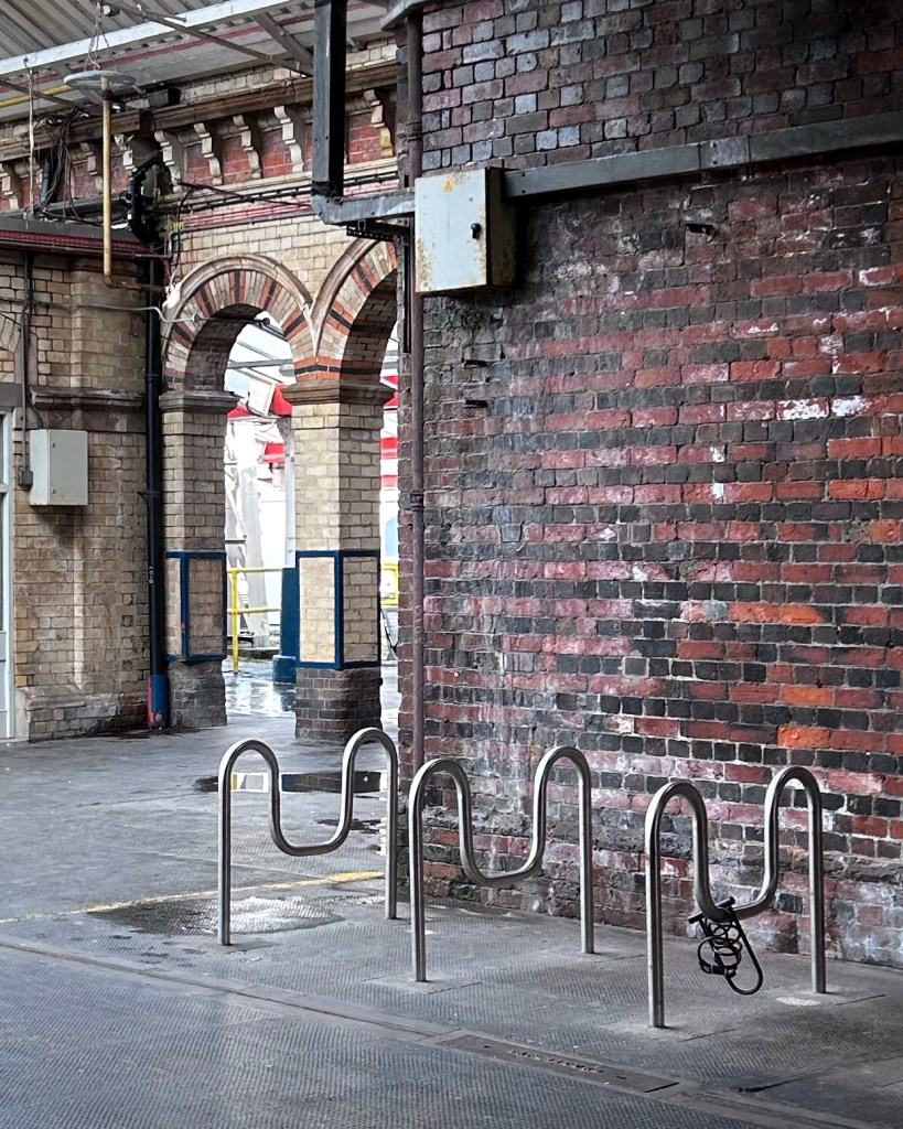 Bicycle stands next to a brick wall and arches on a train station platform.